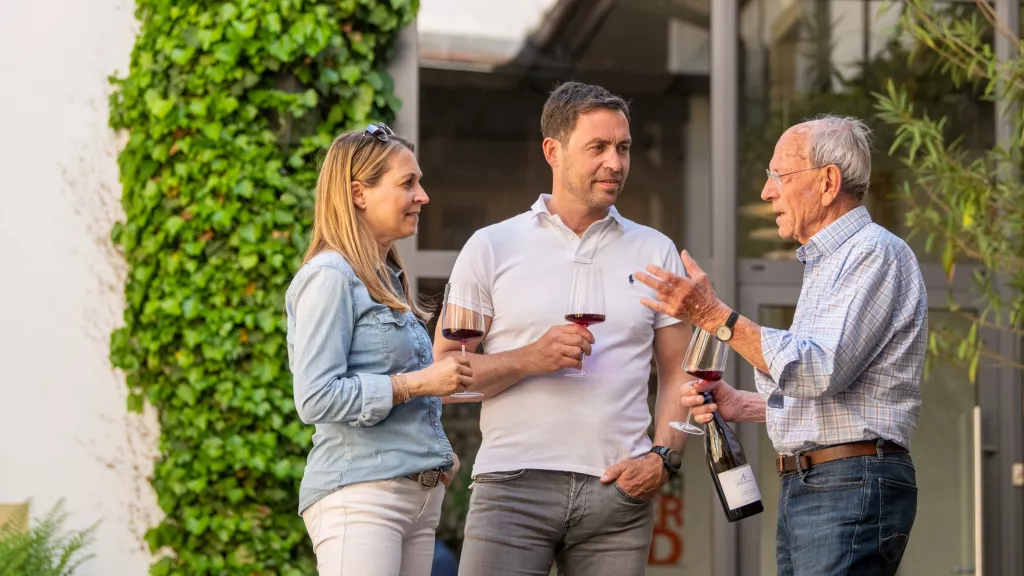 drei Personen stehen vor einem Weingut in der Pfalz und fachsimpeln über Wein