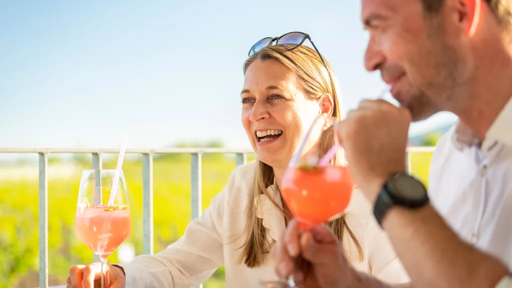 ein Mann und eine Frau trinken Cocktail im Hintergrund sind Pfälzer Weinberge zu sehen