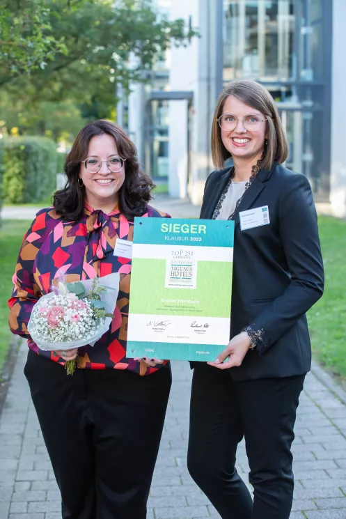 Kloster Hornbach-Top 50 Hotel in der Kategorie Klausurhotel 2023 (© Lina Nikelowski) zwei junge Frauen halten die Auszeichnung Top50 Klausurhotel in ihren Händen